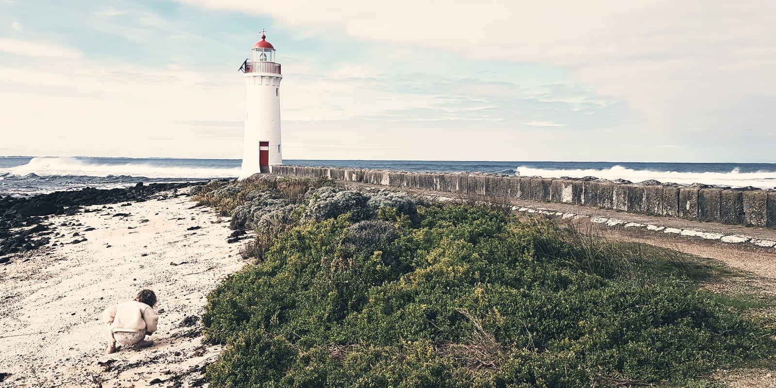 The Port Fairy lighthouse on Griffiths Island, with a child looking for shells on the beach